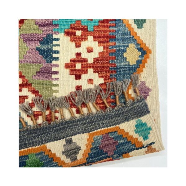 Tapete kilim artesanal com padrões geométricos e franjas em tons terrosos e joia.