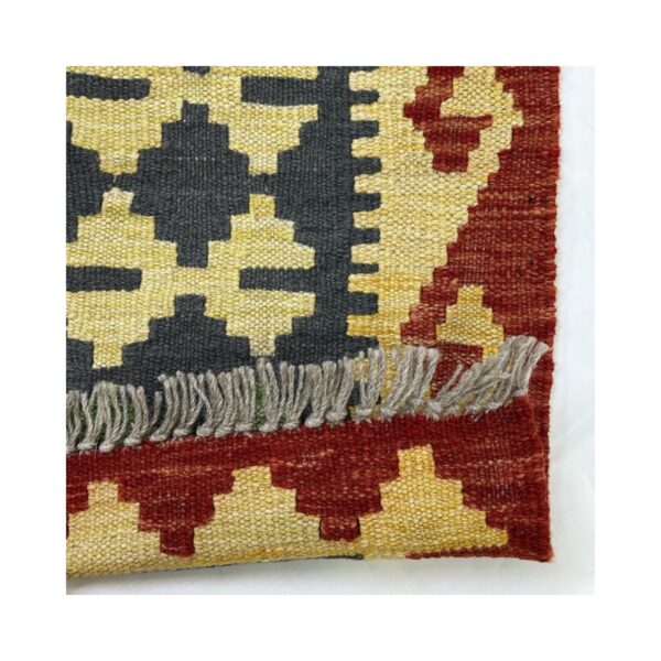 Tapete artesanal com design geométrico e franjas, em tons de amarelo, cinza e vermelho.