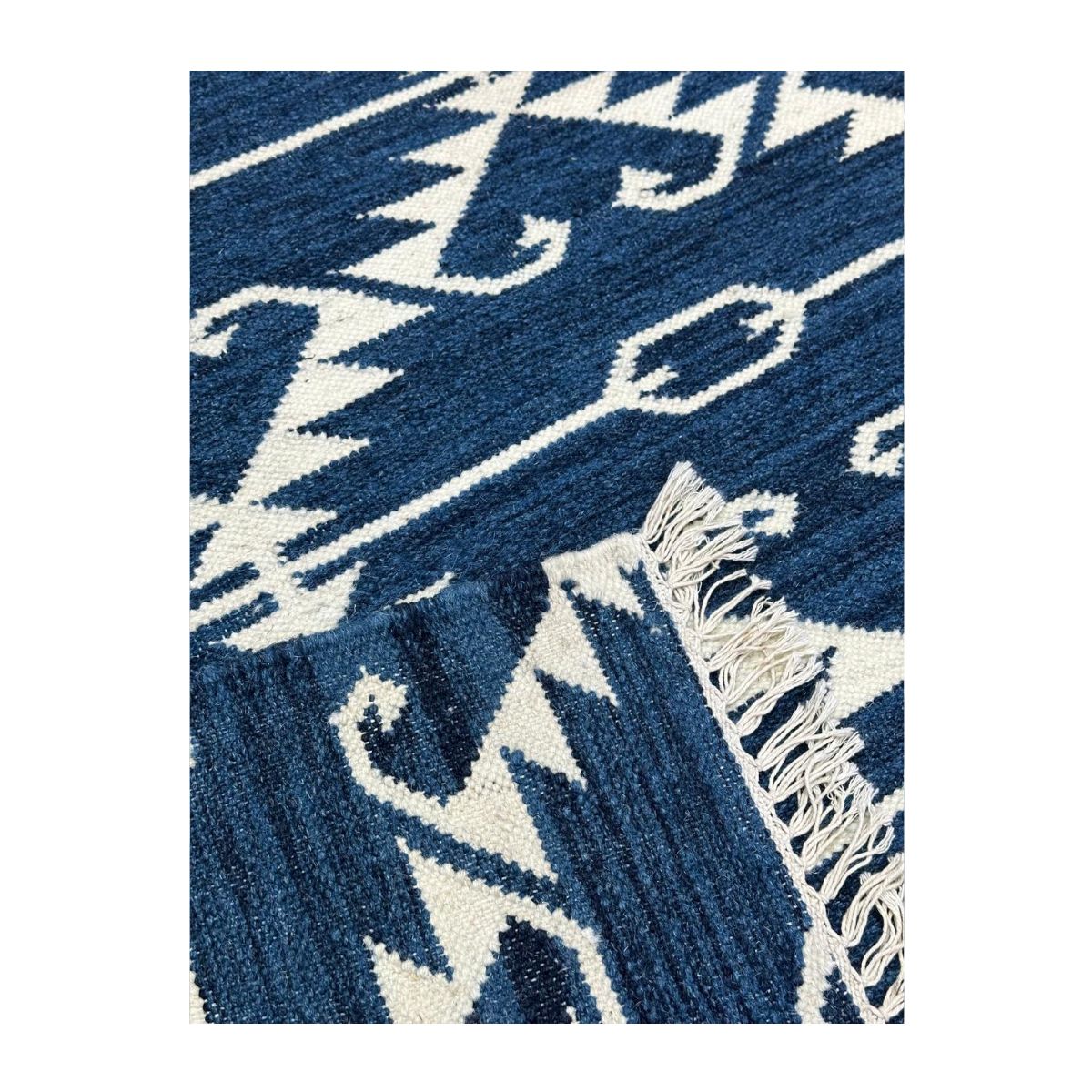 Tapete artesanal azul com padrão geométrico branco e franja.