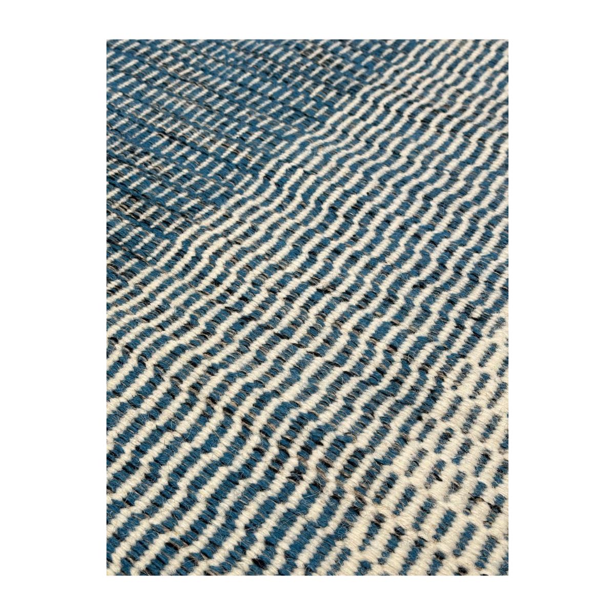 Detalhe de tapete artesanal em azul profundo e branco cremoso com padrão ondulado.